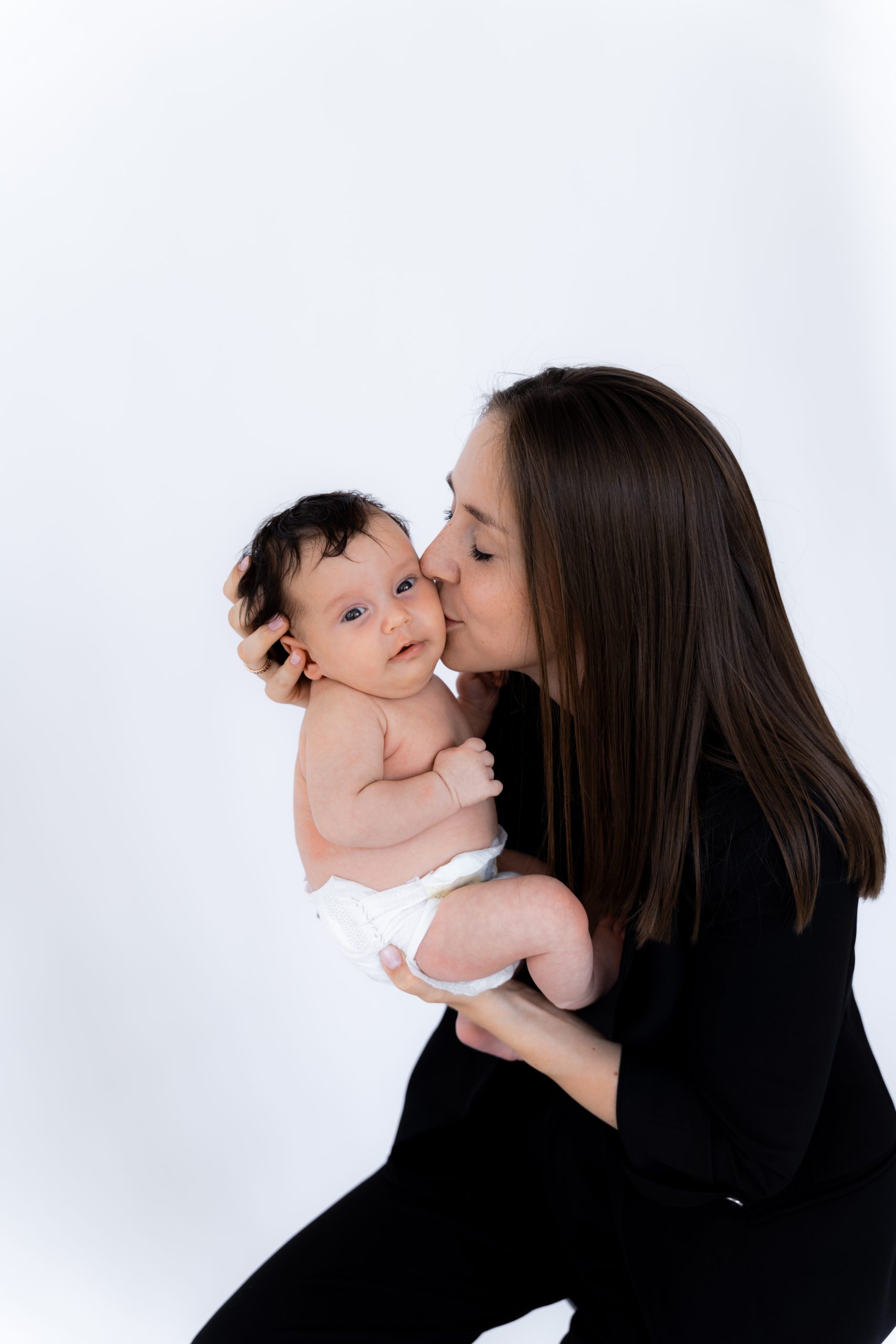 Maminka líbá své novorozené miminko během focení v HLight Studio. Fotograf Lukáš Vavřinec zachytil něžný moment plný lásky a blízkosti